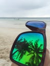 Reflection of palm trees in mirror sunglasses in front of sandy beachline on paradise island. Royalty Free Stock Photo