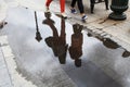 Reflection of people in a puddle on a footpath during rainy weather.