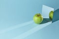 The apple is green, a square mirror on a blue background, a reflection of an apple and from shadows in a mirror.