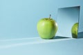 The apple is green, a square mirror on a blue background, a reflection of an apple and from shadows in a mirror.