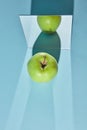 Top view an apple is green, a square mirror on a blue background, a reflection of an apple and from shadows in a mirror. Royalty Free Stock Photo