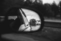 The reflection of road in the side view mirror with raindrops. Travel concept. Bad weather and grey sky Royalty Free Stock Photo