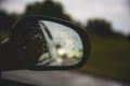 The reflection of road in the side view mirror with raindrops. Travel concept. Bad weather and grey sky Royalty Free Stock Photo