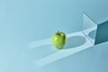 The apple is green, a square mirror on a blue background, a reflection of an apple and from shadows in a mirror.