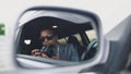 Reflection in side mirror of Paparazzi man sitting inside car and photographing with dslr camera Royalty Free Stock Photo