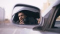 Reflection in side mirror of young private detective man sitting inside car and photographing with dslr camera Royalty Free Stock Photo