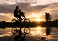 Reflection Silhouette of Father with his toddler on bicycle against the sunset.