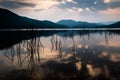 Reflection of sky, cloud, and mountains on very clear surface of the lake and pricky wood weed in the water at a park with rays of