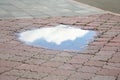 Reflection of sky in puddle on street tiles outdoors