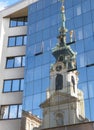 Reflection of Stiftskirsche tower with the clock seen on glass wall modern building