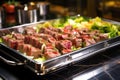 reflection of succulent beef skewers in shiny metal tray