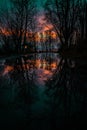 Reflection of a sunset, on the water's surface, with a small cabin on the lake's coast in a forest