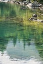 Reflection of treetops and mountain ranges in a turquoise-colored mountain lake with a rocky shore Royalty Free Stock Photo