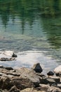 Reflection of treetops and mountain ranges in a turquoise-colored mountain lake with a rocky shore Royalty Free Stock Photo