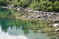 Reflection of treetops and mountain ranges in a turquoise-colored mountain lake with a rocky shore Royalty Free Stock Photo