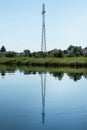 Reflection in the water of a power transmission tower. Natural background with river and green shore Royalty Free Stock Photo