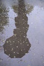 reflection of a woman with an umbrella on wet pavement during rain.