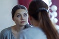 Reflection of a young attractive caucasian woman looking into a mirror. Wearing casual, beautiful blue eyes, serious look.