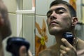 Reflection of young man in mirror shaving with electric shaver Royalty Free Stock Photo