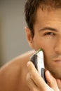 Reflection of young man in mirror shaving with electric shaver Royalty Free Stock Photo