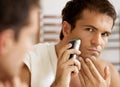 Reflection of young man in mirror shaving with electric shaver Royalty Free Stock Photo