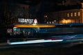 Evening lights of Budapest: Reflective city architecture illuminated by bus stop and passing bus at bus stop in Hungary.