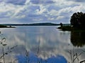 Reflections of gentle white clouds over land extend out into the blue lake