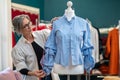 Woman with measure thoughtfully looking at blouse on dummy