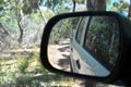 Reflections in a side view mirror of a car driving in the bush.