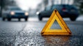 Reflective emergency warning triangle placed on wet road surface with blurred cars in the background signaling caution during Royalty Free Stock Photo