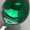 A reflective metal spoon is angled to catch overhead light, creating a green-tinted Royalty Free Stock Photo