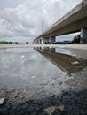 reflective pool of water on the asphalt street beneath the bridge crossing.