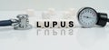 On a reflective white surface lies a stethoscope and cubes with the inscription - LUPUS