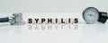 On a reflective white surface lies a stethoscope and cubes with the inscription - SYPHILIS