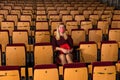 Reflective woman in protective mask sitting alone in empty cinema house