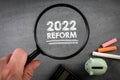 2022 Reform. Medicine, education, taxation and business concept. Magnifying glass on a chalkboard background