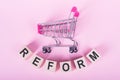 REFORM - word on wooden cubes, on a pink background with a shopping trolley Royalty Free Stock Photo