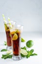 Refreshing alcohol beverage cuba libre with cola, ice, mint, lime, straw in two wet long glasses in modern white kitchen interior, Royalty Free Stock Photo