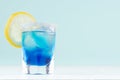 Refreshing alcohol drink blue Hawaii in misted elegant shot glass with ice cubes, citrus slice, salt rim in modern pastel mint.
