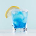 Refreshing alcohol drink blue Hawaii in misted rich shot glass with ice cubes, lemon slice, salt rim in modern pastel mint color.