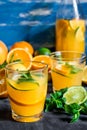 Refreshing beverage, citrus lemonade oranges lime fresh mint in bottle and glasses, sliced fruits on wood table, blue background Royalty Free Stock Photo