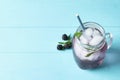 Refreshing blackberry drink with rosemary and ice cubes in mason jar on turquoise wooden table. Space for text