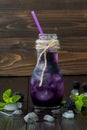 Refreshing blackberry juice in vintage eco style bottle on rustic dark wooden table. Cold summer berry drink with ice and mint. Co