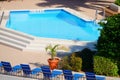 Refreshing blue swimming pool with deck chairs and green plants