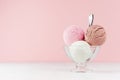 Refreshing classic white, pink, brown ice cream balls in glass bowl with silver spoon on white wooden table and soft light pink.