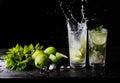 Refreshing cocktail mojito lemonade with splashes, lime and mint on the table. Black background. Close-up.