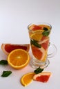 Refreshing cocktail with slices of fresh orange and grapefruit with green mint leaves on white background. Detox citrus cocktail.