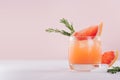 Refreshing cold citrus cocktail with ice cubes, green rosemary and slice grapefruit on soft light pink and white background. Royalty Free Stock Photo