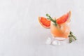 Refreshing cold citrus cocktail with ice cubes, green rosemary and slice grapefruit on soft light white wood background. Royalty Free Stock Photo