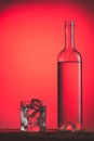 Refreshing cold drink in bottle with drops, and glass with ice on red background. Iced refreshing drinks concept Royalty Free Stock Photo